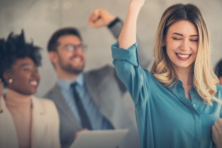 A group of professionals raising their arms in celebration during a workplace achievement