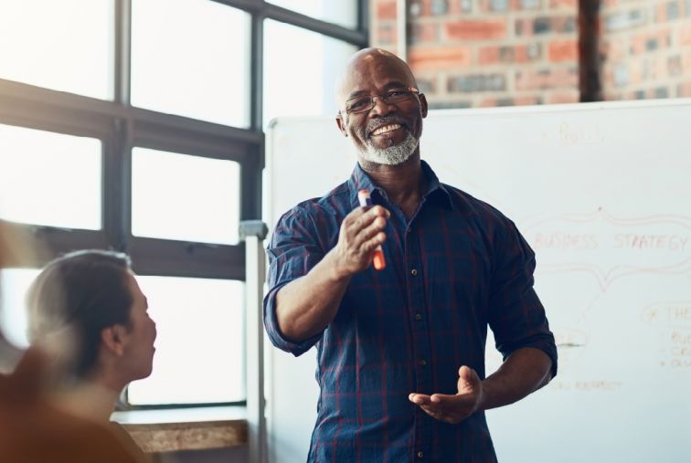 Business leader facilitating a team discussion in a modern office, presenting ideas on a whiteboard during a workplace meeting