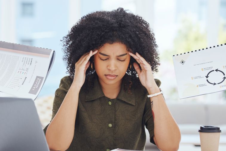 Person working at a desk with a laptop while reviewing documents and charts, illustrating workplace workload and team demands.