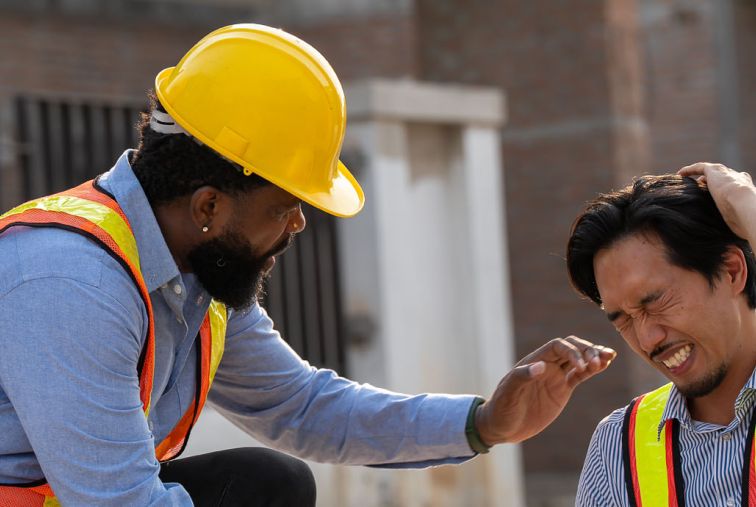 Two workers in safety vests at a construction site, with one worker providing support to another following a workplace injury.